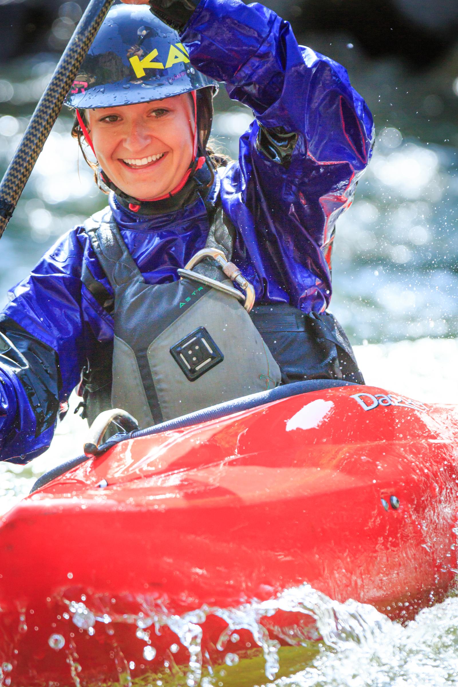 Smiling kayaker in a helmet and dry top paddling through whitewater