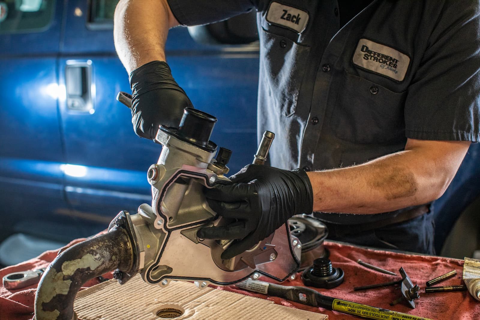 A mechanic's gloved hands rebuilding a diesel part beside a blue truck, lit like a brand campaign