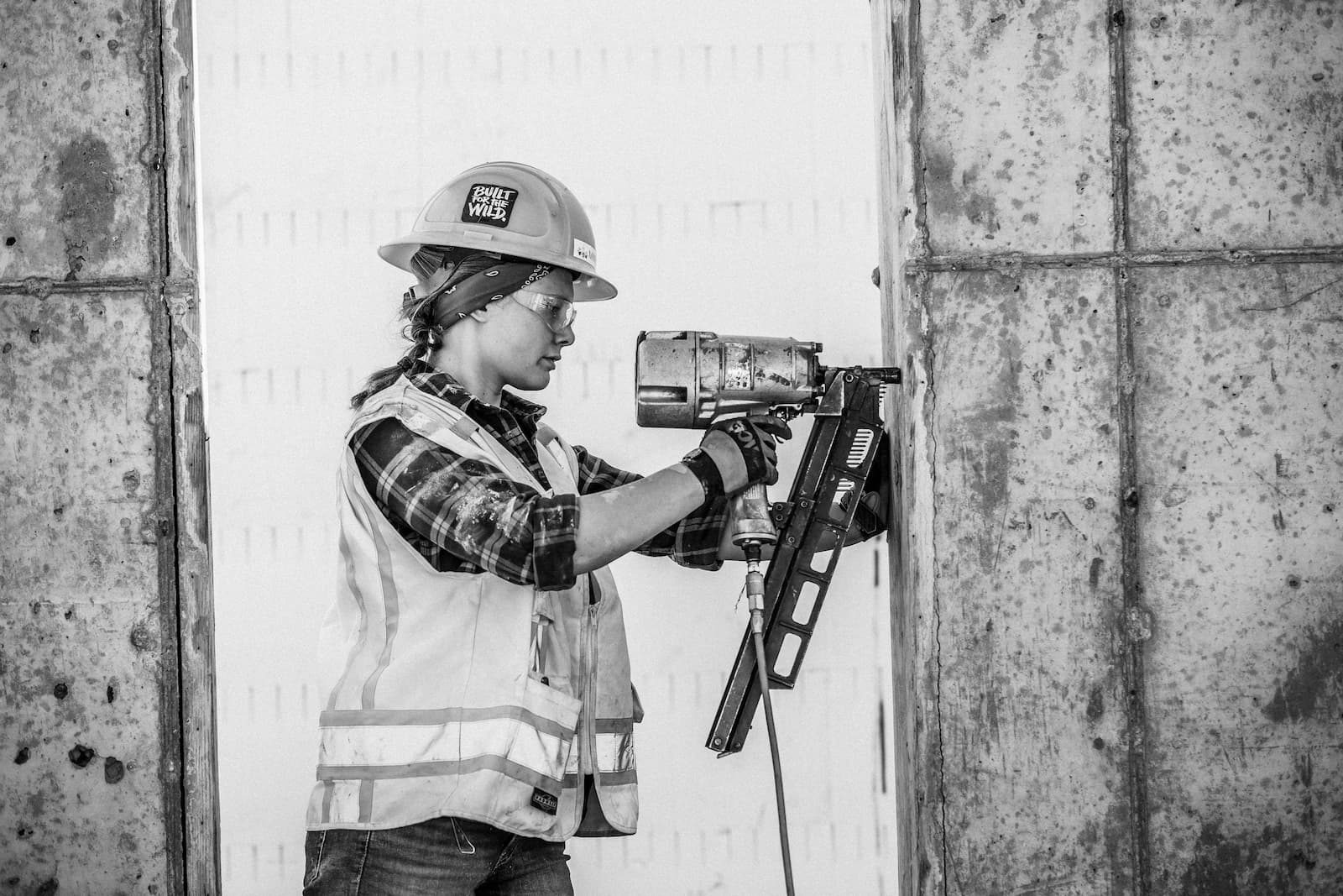 Contractor in a hard hat and safety vest drilling into a concrete wall, black and white
