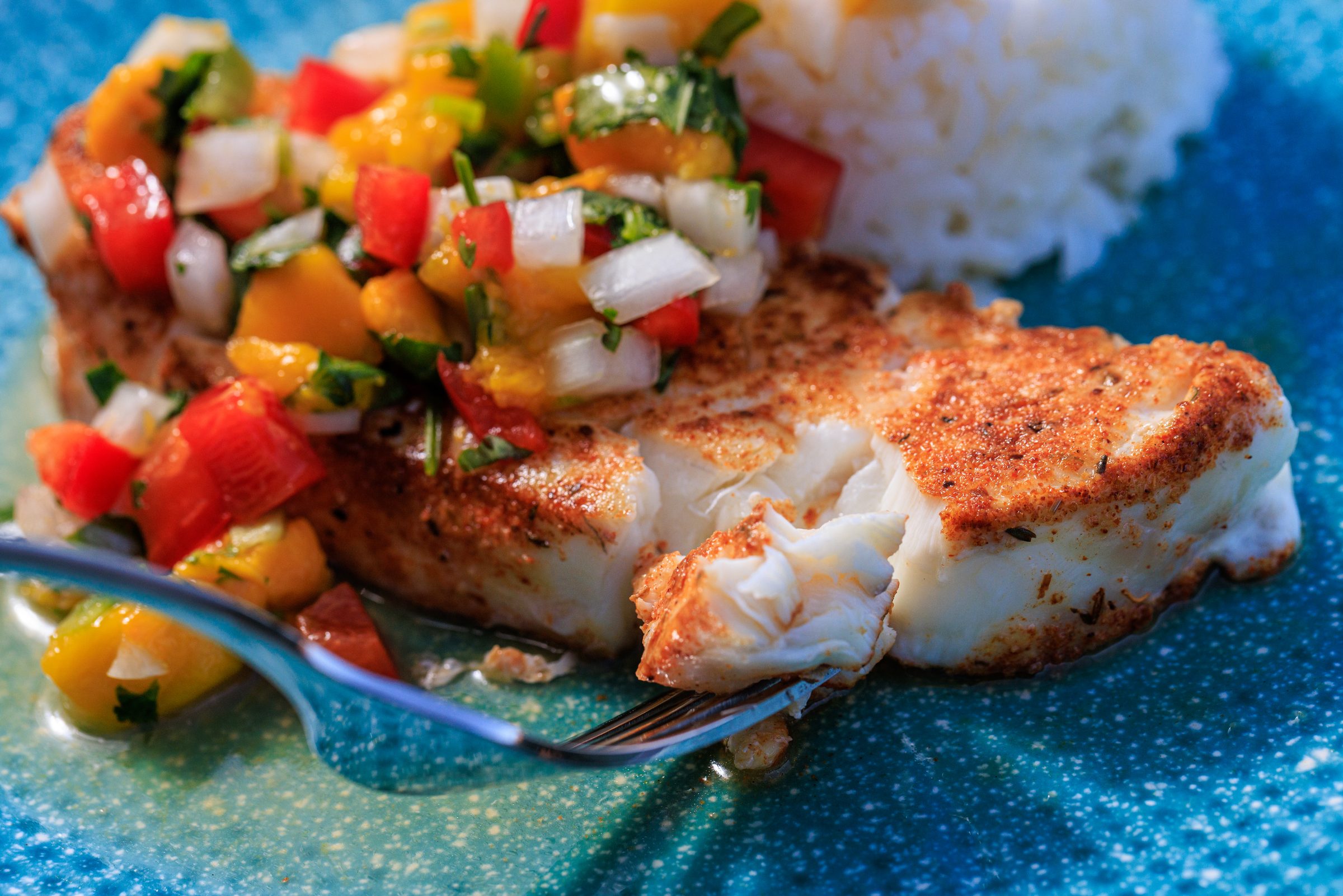 Seared fish with fresh mango salsa and rice on a blue plate