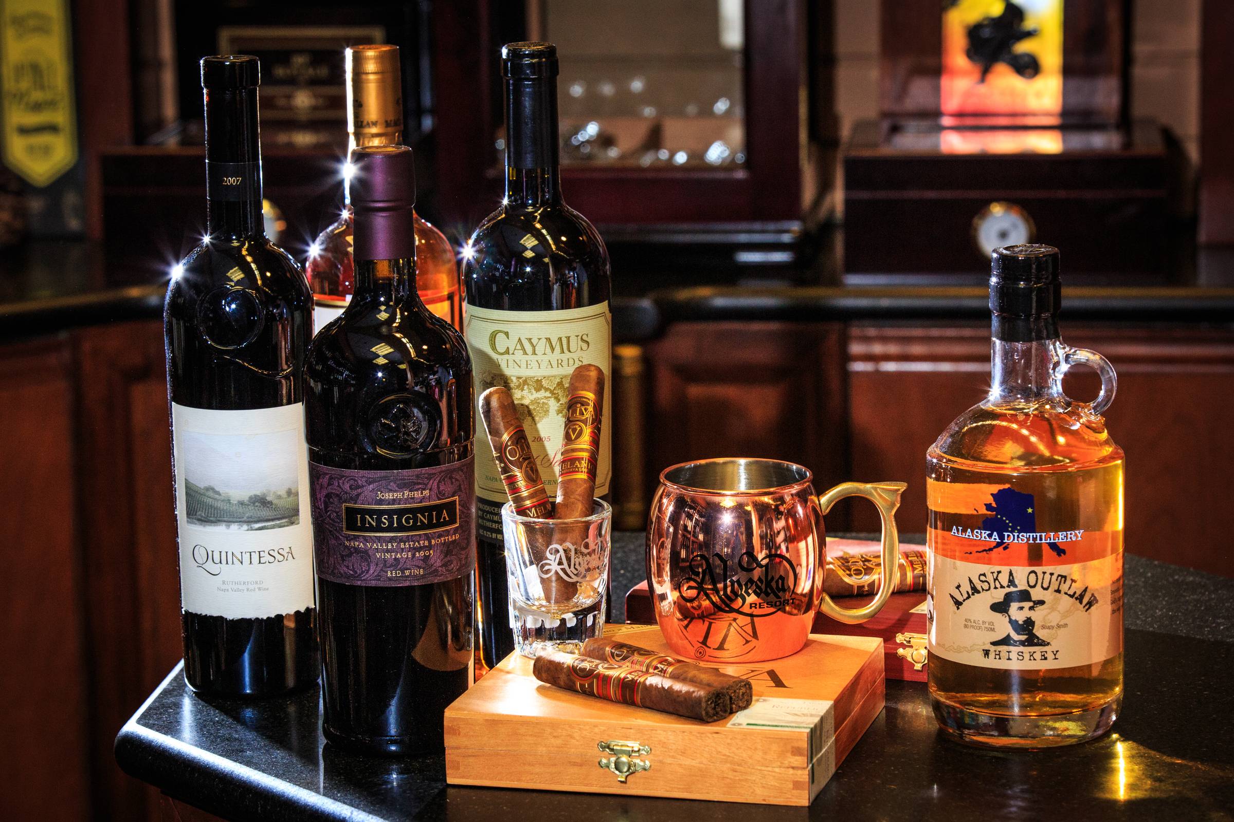 Wine and whiskey bottles with a copper mug on a dark wooden bar